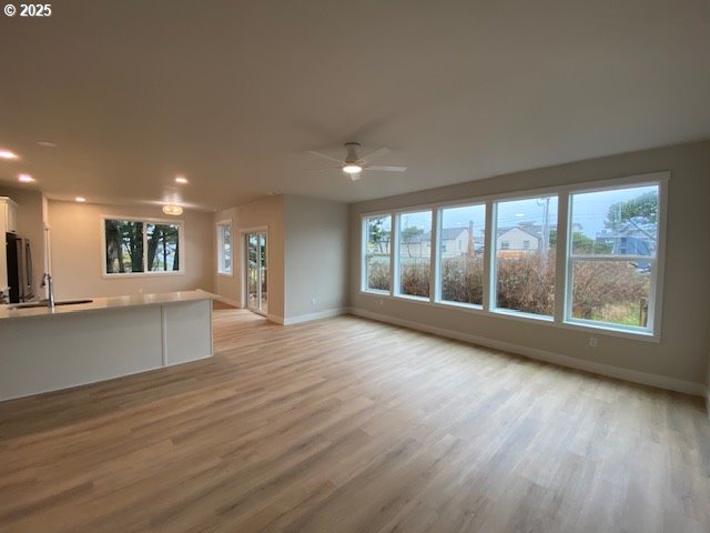 unfurnished living room featuring baseboards, a sink, light wood finished floors, a ceiling fan, and recessed lighting