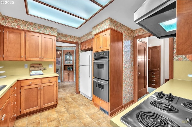 kitchen with multiple ovens, wallpapered walls, extractor fan, freestanding refrigerator, and stainless steel stovetop