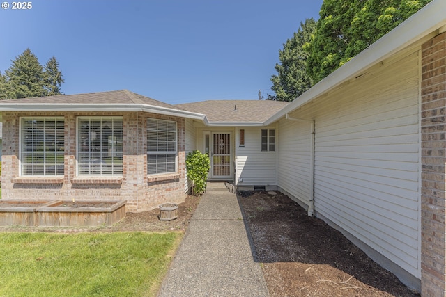 property entrance featuring roof with shingles and brick siding