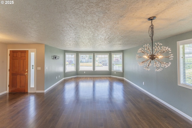 unfurnished living room with a textured ceiling, baseboards, an inviting chandelier, and dark wood-type flooring