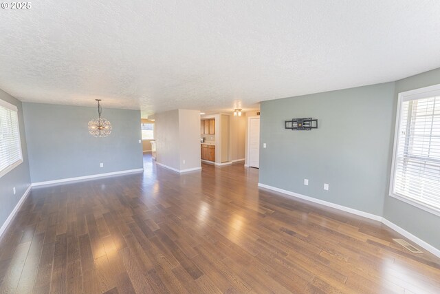 unfurnished living room featuring baseboards, dark wood-style floors, a textured ceiling, and a notable chandelier