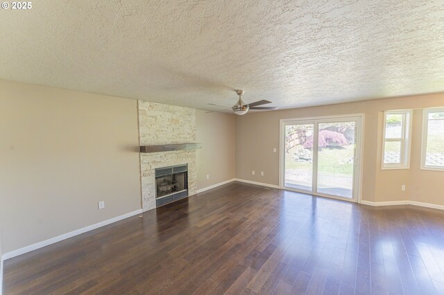 unfurnished living room featuring ceiling fan, a textured ceiling, a fireplace, baseboards, and dark wood-type flooring
