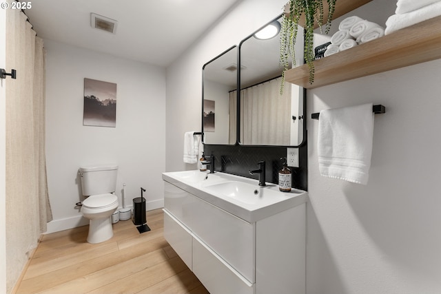full bath with a sink, toilet, baseboards, wood finished floors, and visible vents