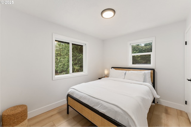 bedroom with baseboards, multiple windows, and light wood-style flooring