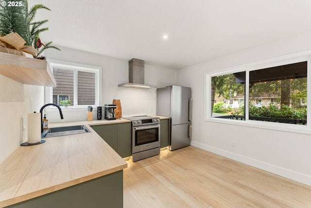 kitchen featuring wall chimney range hood, plenty of natural light, stainless steel appliances, and a sink