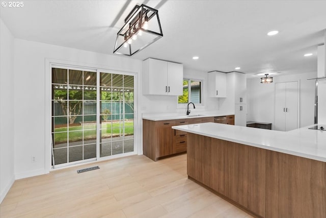 kitchen with light countertops, white cabinets, a sink, brown cabinetry, and recessed lighting