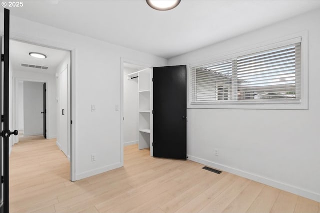 unfurnished bedroom featuring light wood-style flooring, a walk in closet, baseboards, and a closet