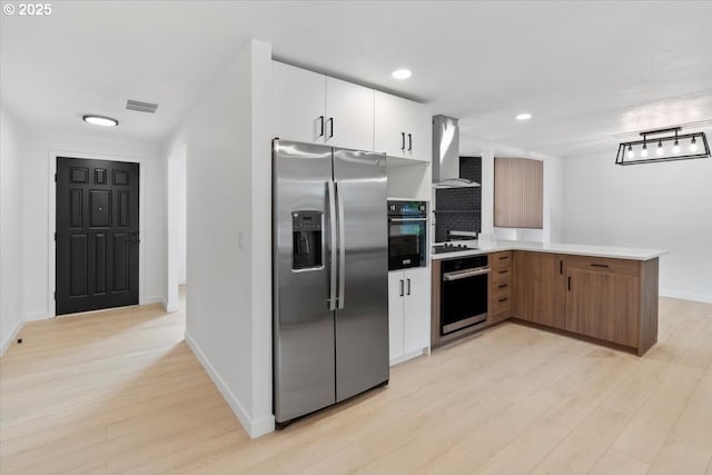 kitchen featuring black appliances, wall chimney range hood, light wood-style floors, a peninsula, and baseboards
