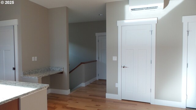 interior space with light wood-type flooring, a wall mounted air conditioner, and baseboards