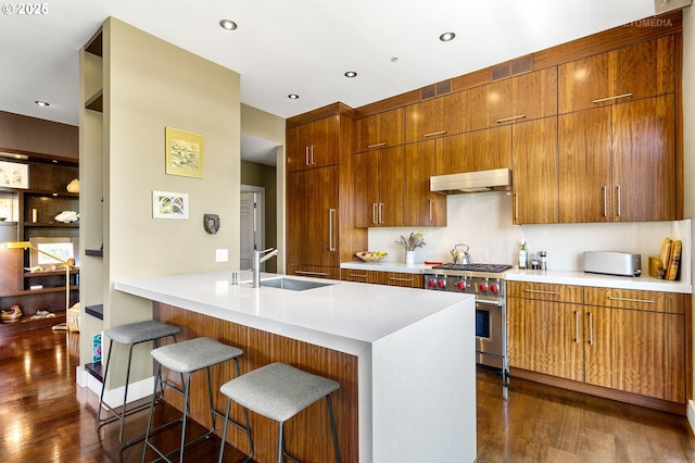 kitchen featuring sink, a breakfast bar area, dark hardwood / wood-style floors, kitchen peninsula, and stainless steel stove