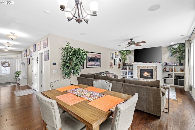 dining area featuring dark wood-type flooring, a glass covered fireplace, and ceiling fan with notable chandelier