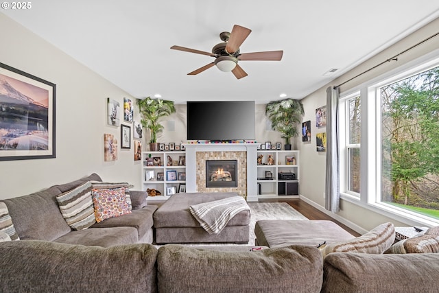 living area with dark wood-style floors, a ceiling fan, visible vents, baseboards, and a tiled fireplace