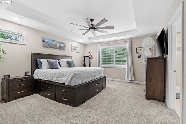 bedroom featuring a ceiling fan, a tray ceiling, recessed lighting, baseboards, and light colored carpet