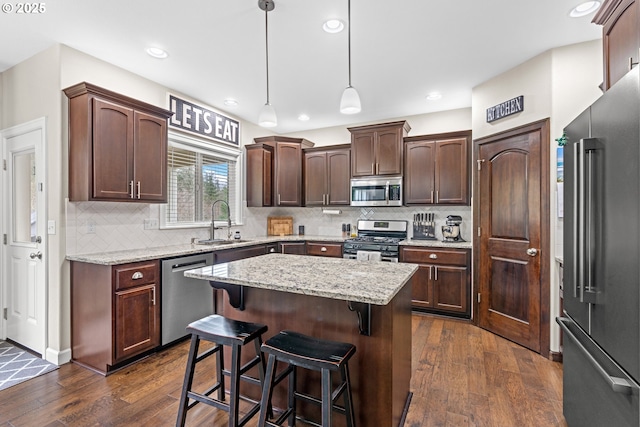 kitchen with dark wood finished floors, a sink, stainless steel appliances, dark brown cabinetry, and a center island