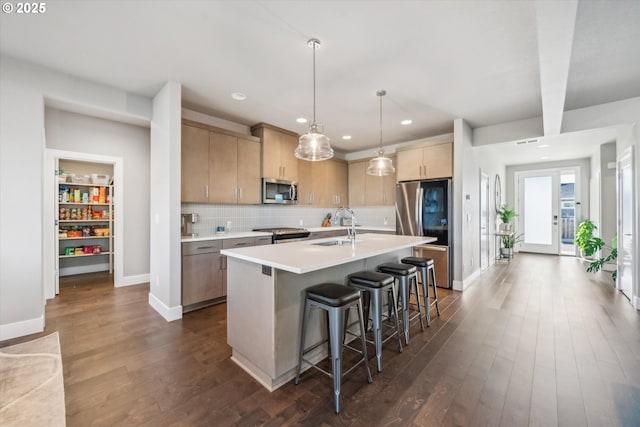 kitchen with light brown cabinetry, decorative light fixtures, an island with sink, dark hardwood / wood-style flooring, and stainless steel appliances