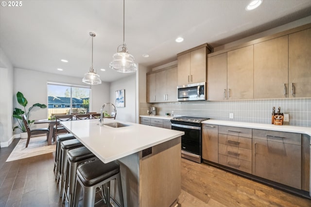 kitchen with appliances with stainless steel finishes, sink, a center island with sink, and light brown cabinets