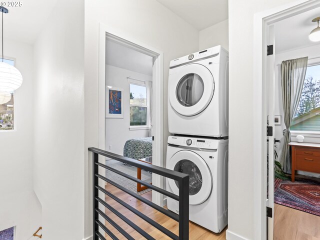 laundry area with plenty of natural light, stacked washing maching and dryer, and light wood-type flooring