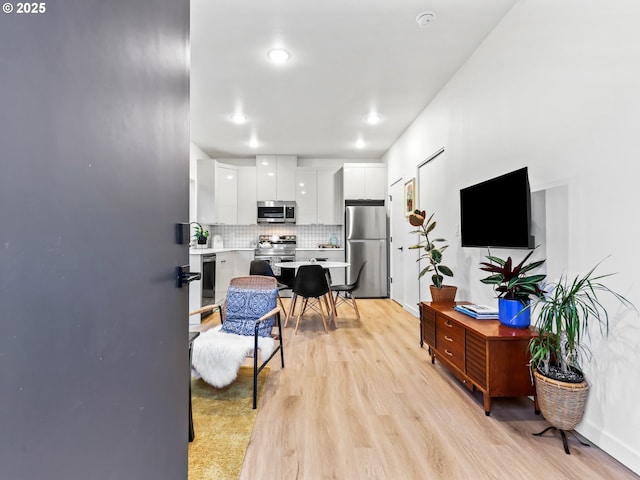 kitchen with stainless steel appliances, white cabinetry, tasteful backsplash, and light hardwood / wood-style flooring