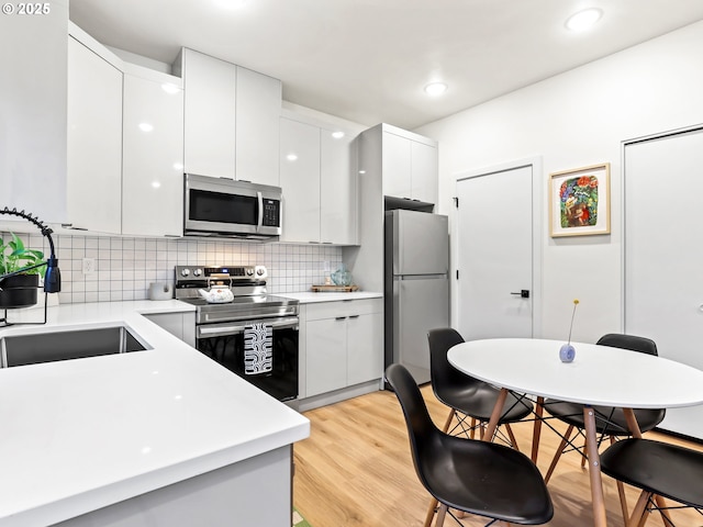 kitchen featuring white cabinetry, sink, stainless steel appliances, light hardwood / wood-style floors, and decorative backsplash