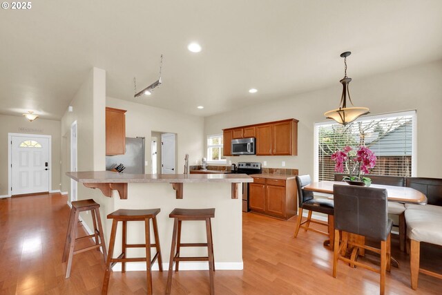 kitchen featuring pendant lighting, a breakfast bar, stainless steel appliances, kitchen peninsula, and light wood-type flooring