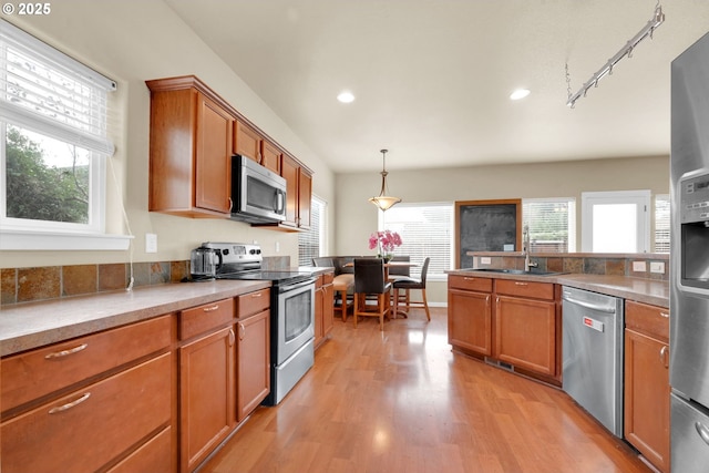 kitchen with appliances with stainless steel finishes, sink, pendant lighting, and light hardwood / wood-style flooring