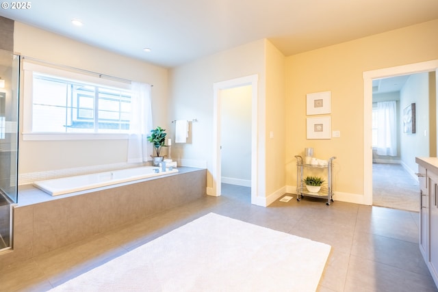 bathroom featuring a healthy amount of sunlight, vanity, tile patterned floors, and tiled tub