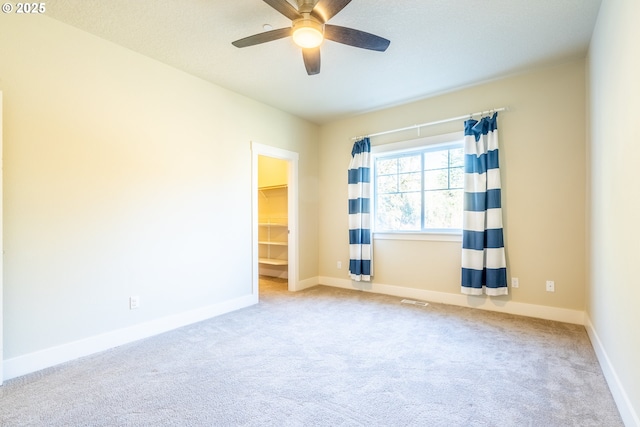 carpeted spare room with visible vents, baseboards, and a ceiling fan