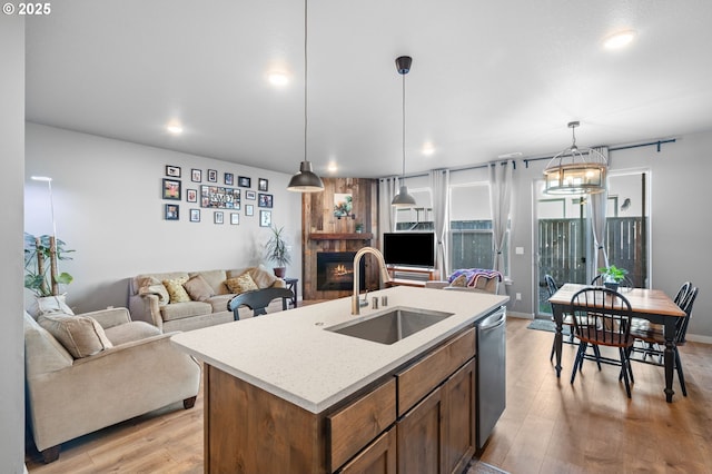 kitchen with light wood-style flooring, a sink, a lit fireplace, stainless steel dishwasher, and hanging light fixtures