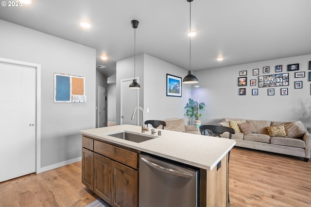 kitchen featuring decorative light fixtures, a center island with sink, light wood-style flooring, stainless steel dishwasher, and a sink