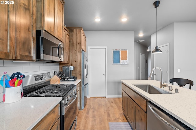 kitchen with stainless steel appliances, brown cabinets, a sink, and light wood-style floors