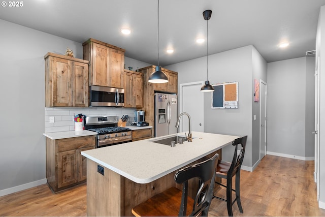 kitchen with appliances with stainless steel finishes, a sink, light wood finished floors, and decorative backsplash