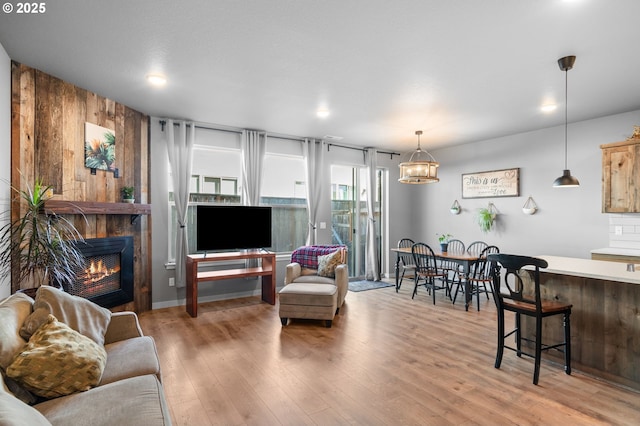 living room with light wood-type flooring, a warm lit fireplace, and wood walls