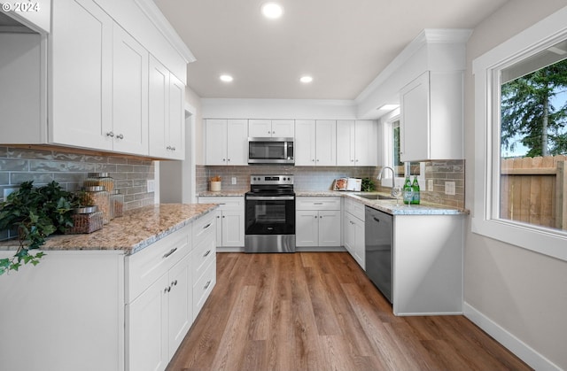 kitchen with light wood finished floors, decorative backsplash, appliances with stainless steel finishes, a sink, and baseboards