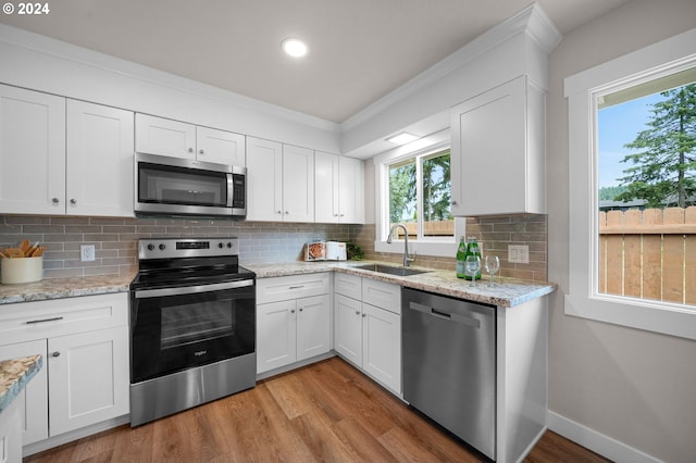 kitchen with white cabinets, decorative backsplash, light wood-style flooring, appliances with stainless steel finishes, and a sink