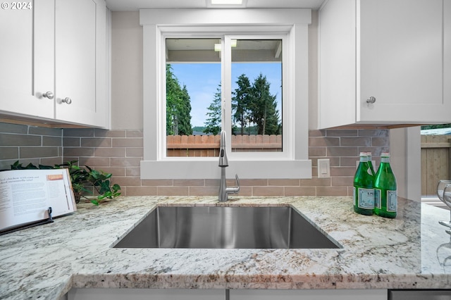 details with light stone counters, white cabinetry, a sink, and tasteful backsplash