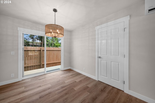 unfurnished dining area featuring an inviting chandelier, wood finished floors, visible vents, and baseboards