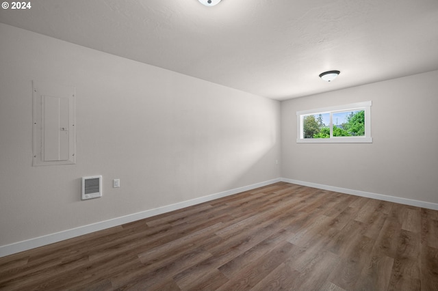 spare room featuring electric panel, baseboards, and wood finished floors