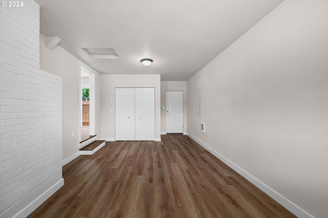 unfurnished bedroom with dark wood finished floors, a closet, attic access, brick wall, and baseboards