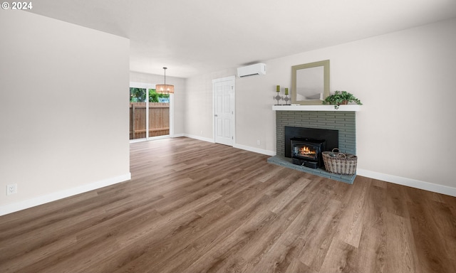 unfurnished living room featuring a brick fireplace, a wall unit AC, baseboards, and wood finished floors