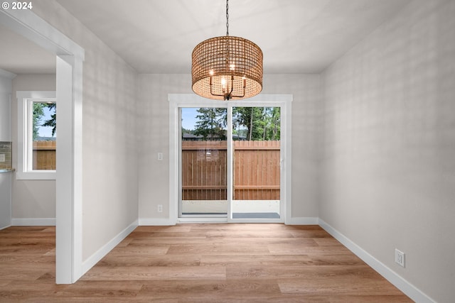 unfurnished dining area with light wood-style floors, plenty of natural light, baseboards, and an inviting chandelier