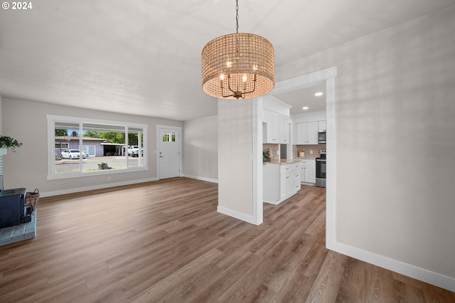 unfurnished living room featuring recessed lighting, wood finished floors, baseboards, a wood stove, and an inviting chandelier