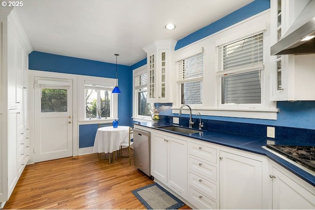 kitchen featuring white cabinets, dark countertops, stainless steel appliances, wall chimney range hood, and a sink