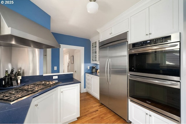 kitchen with appliances with stainless steel finishes, dark countertops, white cabinets, and wall chimney exhaust hood