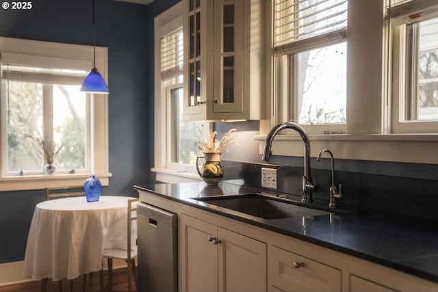 kitchen featuring decorative light fixtures, a sink, stainless steel dishwasher, dark countertops, and glass insert cabinets