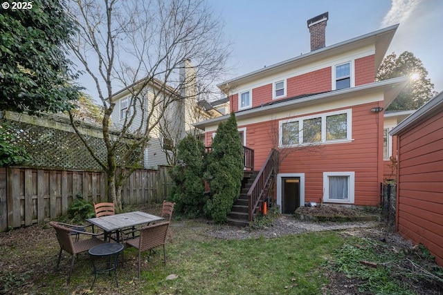 rear view of house with fence, stairs, a lawn, outdoor dining space, and a chimney