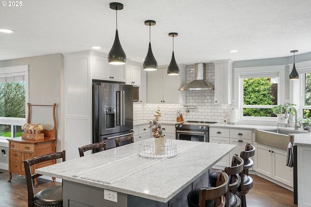 kitchen with high end appliances, dark wood-style floors, wall chimney exhaust hood, a breakfast bar area, and a sink