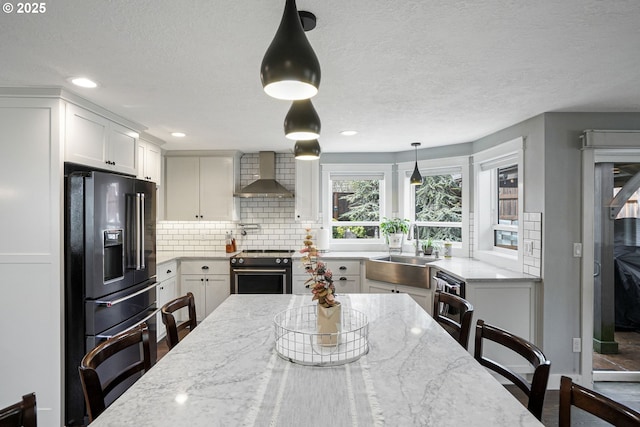 kitchen featuring white cabinets, decorative backsplash, wall chimney exhaust hood, decorative light fixtures, and black appliances