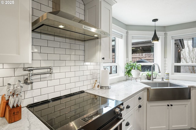 kitchen featuring electric range, backsplash, white cabinets, a sink, and wall chimney range hood