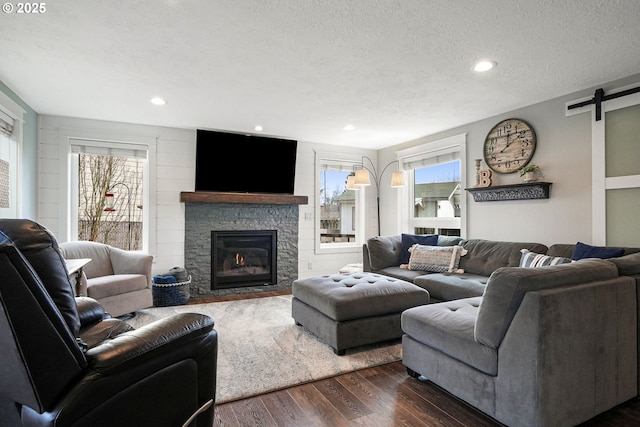 living area featuring a textured ceiling, a stone fireplace, a barn door, recessed lighting, and dark wood-style floors