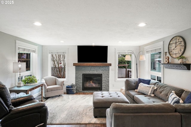 living area featuring recessed lighting, a textured ceiling, wood finished floors, and a stone fireplace